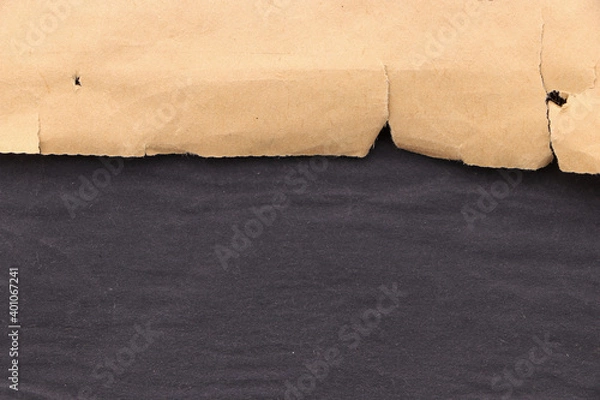 Fototapeta Edge of torn yellowed paper on a black surface. Black blank background.