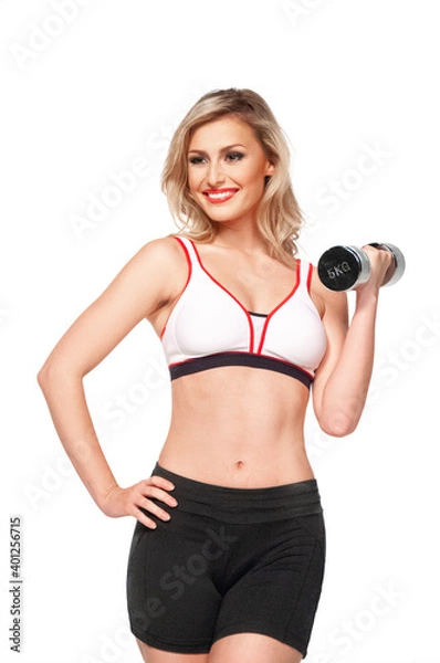 Fototapeta Portrait of a fit, young white female athlete with curly long blond hair posing by herself holding a dumbbell in a studio with white background wearing black shorts & sports bra.