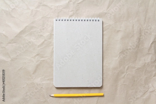 Obraz  Gray notepad with white coiled spring and pencil on a background of beige crumpled craft paper