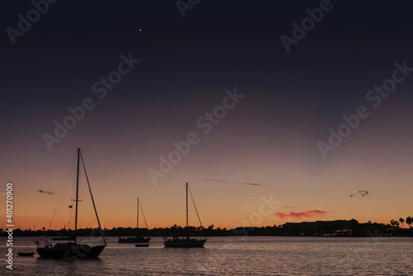 Fototapeta Moored sailboats silhouetted against a subtropical sunset with the planets Jupiter and Saturn aligned in the sky above