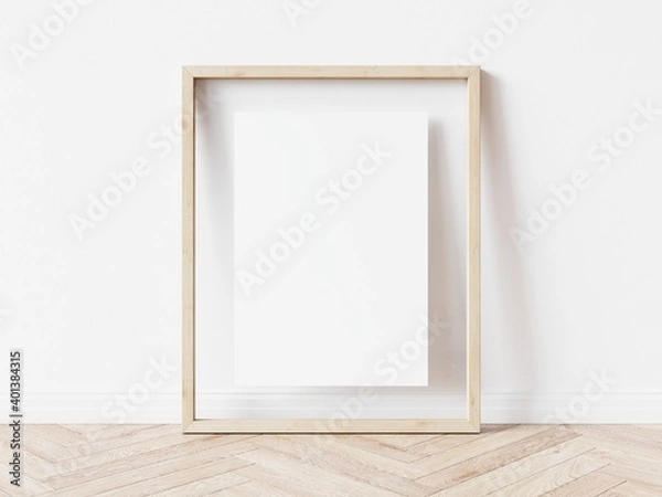 Fototapeta Blank vertically oriented rectangular picture frame with light wood border standing on wooden floor leaning on white wall. 3D Illustration.