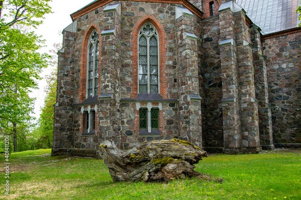 Obraz Latvia - The Cesvaine Lutheran Church, a building of colored stones, a large driftwood on a green lawn.