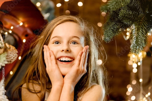 Fototapeta portrait of a beautiful little girl laughing. a child stands near a red car under the snow, New Year's surprise snowfall. concept of happy childhood, making a wish for the new year and birthday.
