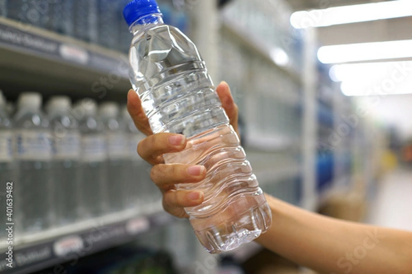 Obraz Close up female hand holding a bottle of drinking water in a grocery store.