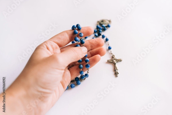 Obraz Blue beaded rosary held by a caucasian young woman's hand on white background.