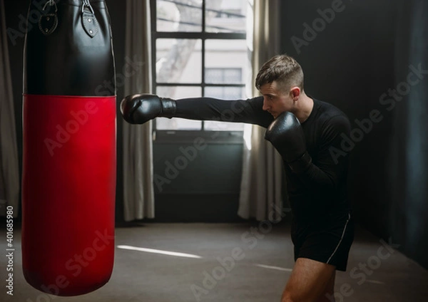 Obraz A young athletic man is hitting a boxing bag. Boxer practicing punches in the ring. The athlete strikes with a punching bag. 4k video