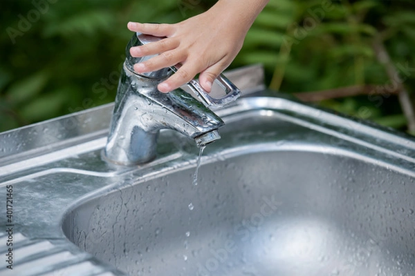 Obraz Baby try to turn off water faucet but water still leak. A child's hand turning off the tap. Save water. World Water Monitoring Day. Environment and health care concept. Natural green background