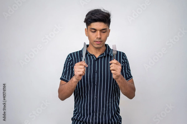 Fototapeta portrait of young boy looking into the fork and also holds a fork and a spoon against a white background.