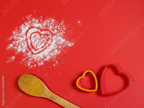 Obraz Bakery products. Flour is scattered on the table in the form of hearts. Form for gingerbread. Valentine's day baked goods flour scattered in the shape of a heart on a red background. Christmas 