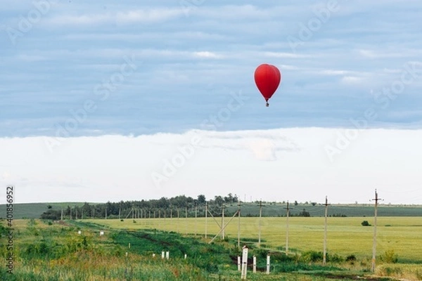 Fototapeta Red hot air balloon in shape of heart is landing on the green field