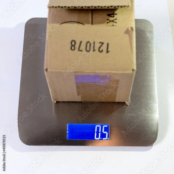 Fototapeta The product in a cardboard box being weighted on a postal weight scale