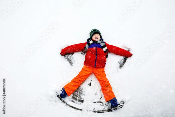 Obraz Cute little kid boy in colorful winter clothes making snow angel, laying down on snow. Active outdoors leisure with children in winter. Happy healthy child having fun and laughing outdoors