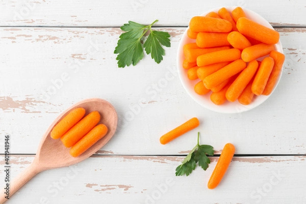 Fototapeta Small peeled pieces of carrot in plate on white wooden table. Top view.