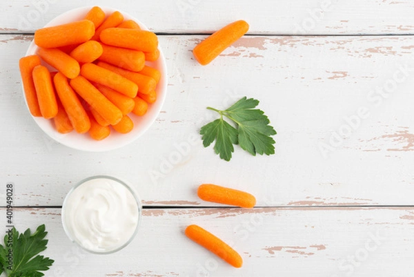 Obraz Small peeled pieces of carrot in plate on white wooden table. Top view. Copy space.