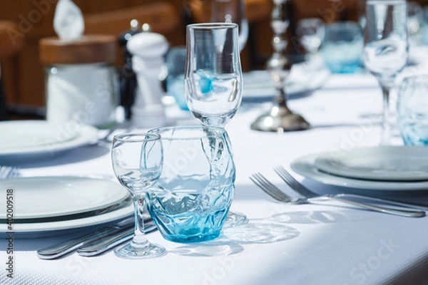 Fototapeta Festive table set, catering with white cloth, plates, forks, blue glasses, salt and pepper pots for wedding, family event or happy birthday party.