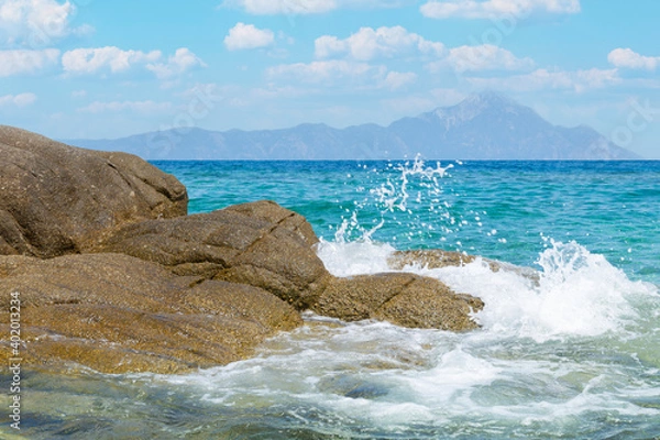 Fototapeta Aegean Sea Blue water waves Crashing on Rocks of Sithonia peninsula of Chalkidiki with Mount Athos on background