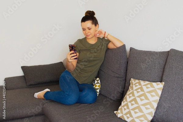 Fototapeta The girl sits on the couch and speaks on the phone. Overall plan