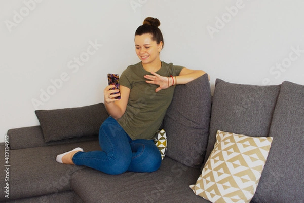 Fototapeta The girl sits on the couch and speaks on the phone. Overall plan