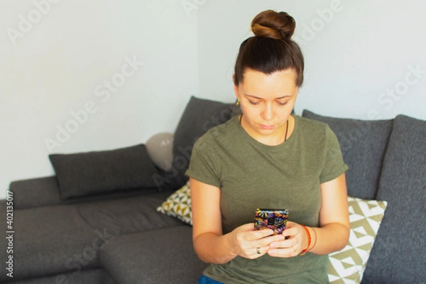 Fototapeta Girl sitting on the couch and writing a message on the phone