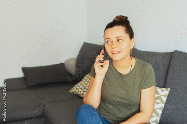 Fototapeta The girl sits on the couch and speaks on the phone