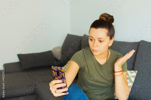 Fototapeta The girl sits on the couch and speaks on the phone. In a bad mood