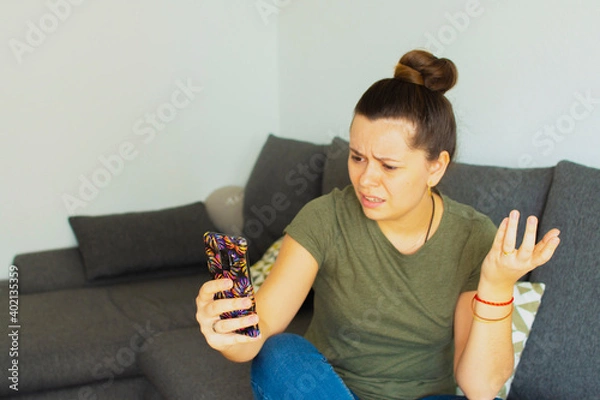 Fototapeta The girl sits on the couch and speaks on the phone. In a bad mood