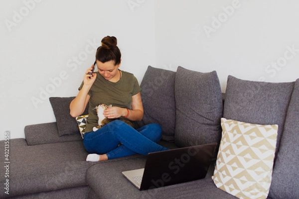Fototapeta Girl at home working on a computer with a cat in her arms