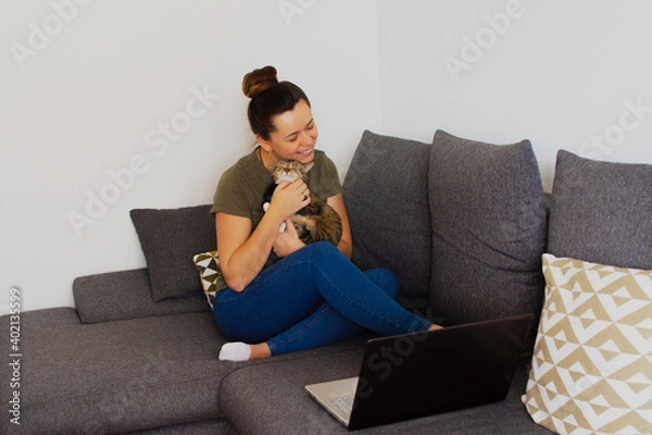 Fototapeta Girl at home working on a computer with a cat in her arms
