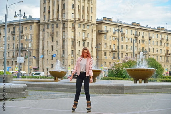 Fototapeta Girl skating on roller skates on the background of high-rise Stalin's building and fountains in St. Petersburg