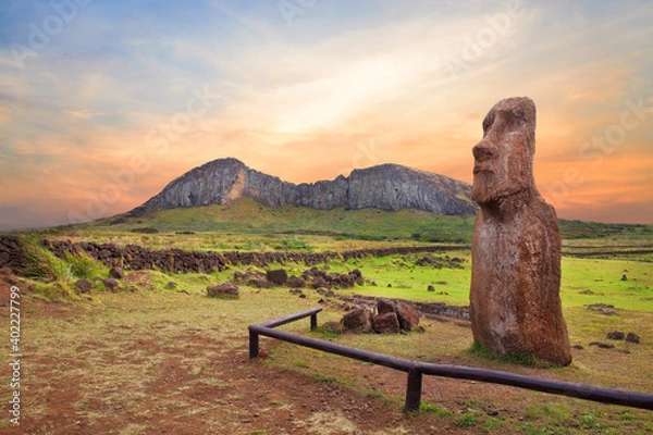 Fototapeta Stone fence and Moai statues at the entrance in the Ahu Tongariki ceremonial center on Easter Island, covered by a colorful sunset sky, against the crater of the Rano Raraku volcano.