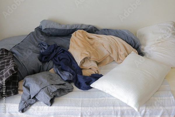Obraz 洋服が散らかった汚い部屋のベットと布団と枕
