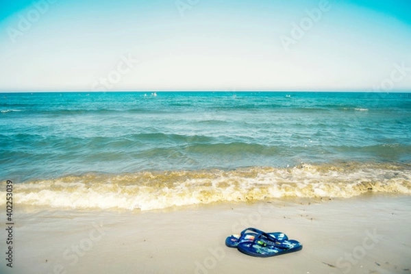 Fototapeta Flip flops on the beach near the blue sea