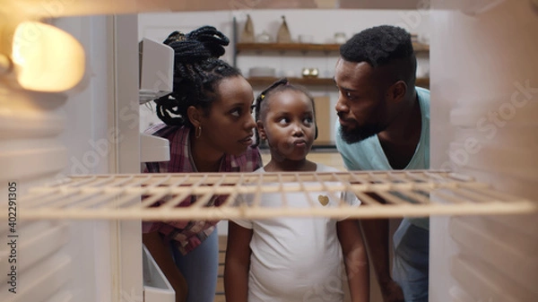 Fototapeta Afro-american hungry family looking into empty fridge at home