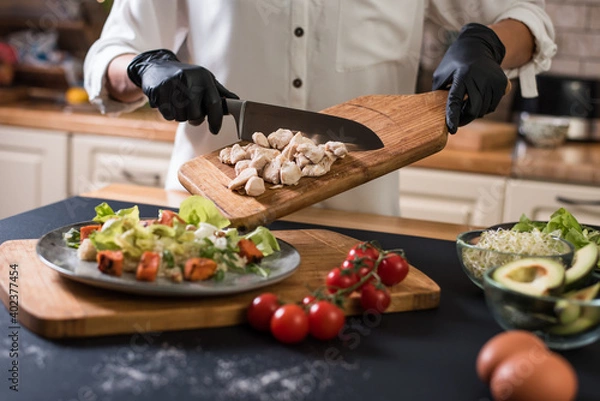 Fototapeta Close up of chef hands with kitchen knife cutting meat on a wooden board