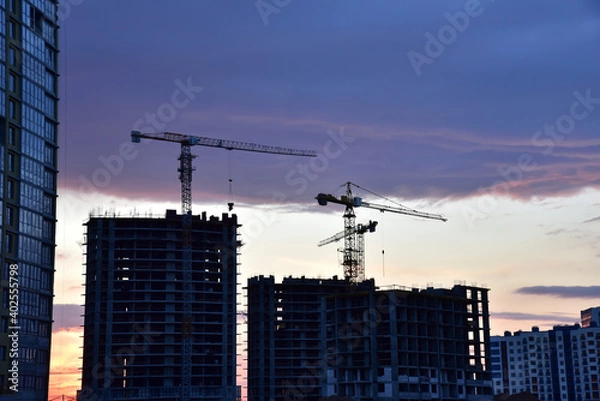 Fototapeta Silhouettes of tower cranes on awesome sunset background. Preparing to pour a bucket of concrete into formwork. Construction a multi-storey residential building. Small sharpness, possible granularity