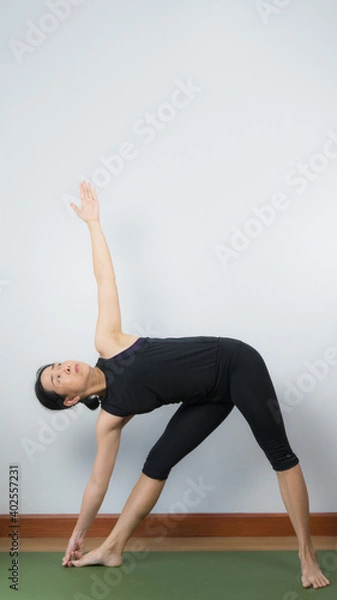 Fototapeta Asian young woman wear a black yoga outfit . Practicing yoga Standing Asanas Action UTTHITA TRIKONASANA (Extended triangle pose).Home yoga practice on white background