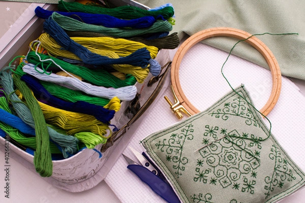 Fototapeta A pillow with embroidery lies next to a box of thread