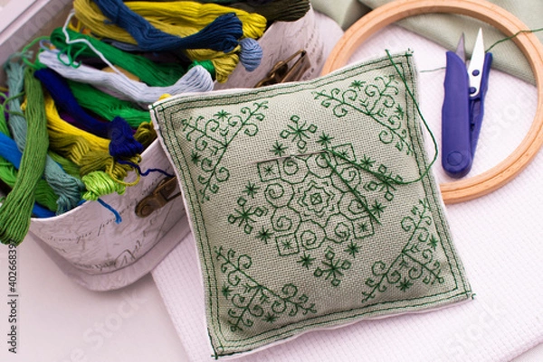 Fototapeta A pillow with embroidery lies next to a box of thread