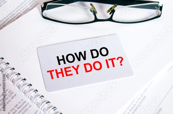 Fototapeta Text How Do They Do it on a business card lying on a notepad with eyeglasses and text documents