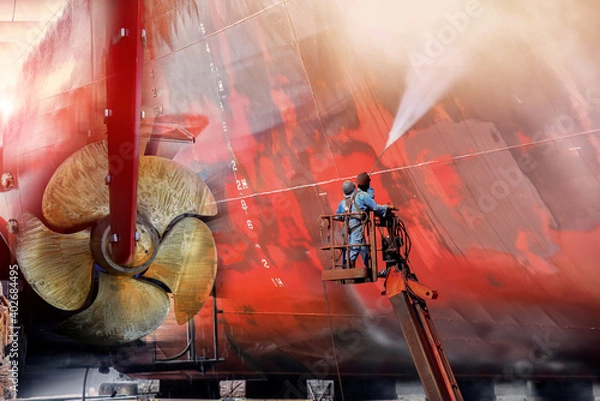 Obraz Worker in dry dock with water jet cleans the bottom of  the cargo ship from sea vegetation and muse colonies during routine overhaul in Shipyard and propeller background