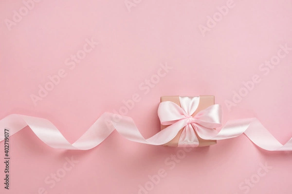 Fototapeta Gift box with long ribbon on pastel pink background. Present for Valentines Day, Mother's Day or Women's Day. Festive monochrome background. Top view flat lay with free space.