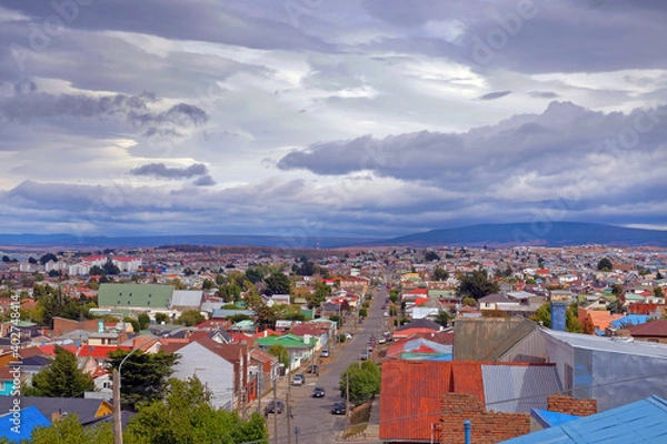 Fototapeta Panoramic view of Punta Arenas, showing colorful roofs, against the ocean covered by a dramatic sky.
