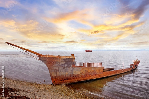 Fototapeta The wreck of the Frigate Lord Lonsdale beached on the shores of Punta Arenas, during a warm sunset, against a colorful sky covered by dramatic clouds.