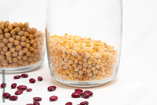 Obraz clear glass jar one quarter filled with peas and a jar of chickpeas in the background out of focus, red beans scattered partially out of focus