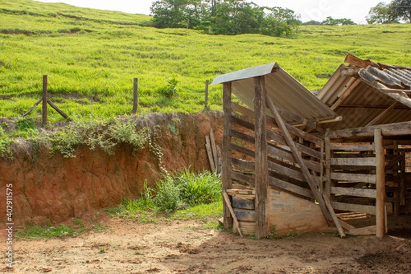 Fototapeta A kind of barn on a corral, after a heavy rain with the ground full of puddles. In the background there are a green pasture and blue sky