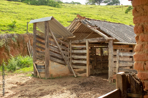 Fototapeta A kind of barn on a corral, after a heavy rain with the ground full of puddles. In the background there are a green pasture and blue sky