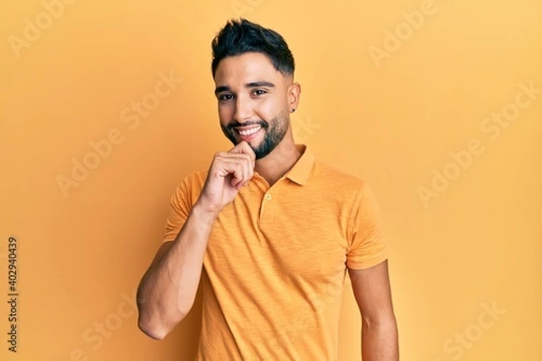 Fototapeta Young man with beard wearing casual clothes smiling looking confident at the camera with crossed arms and hand on chin. thinking positive.