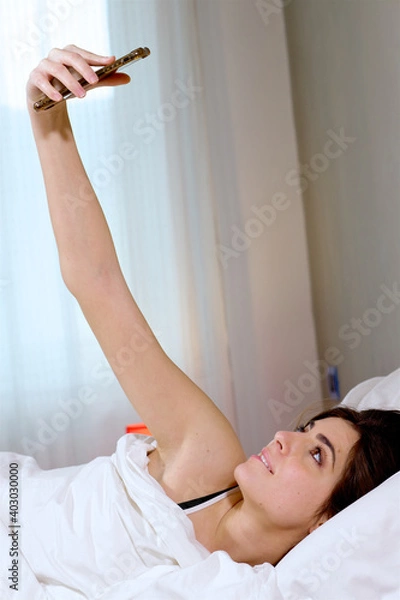 Obraz Happy woman in quarantine at home in bed taking selfie for social network