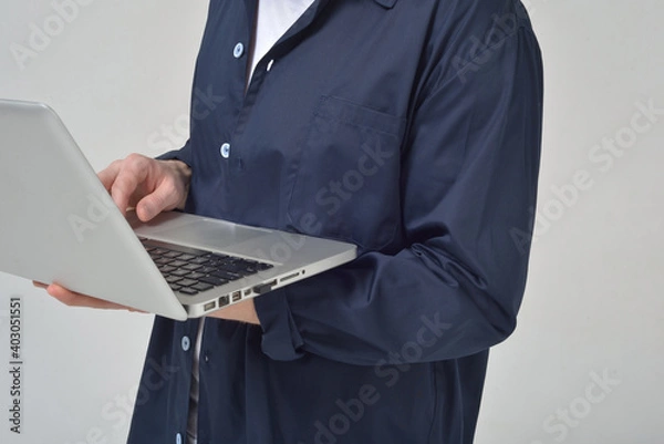 Obraz A man without a face in a blue dressing gown works on a laptop deja in his hands close-up