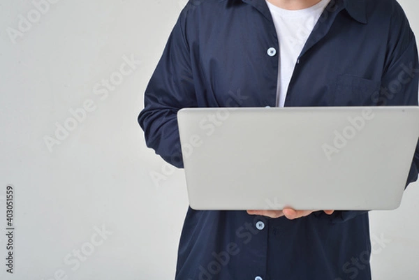 Obraz A man without a face on a white background in the studio holds a laptop in his hands works
